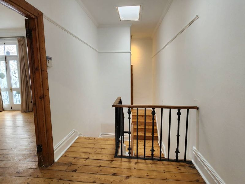 A bright hallway featuring timber flooring, a skylight, and a classic wrought iron balustrade leading to a staircase.