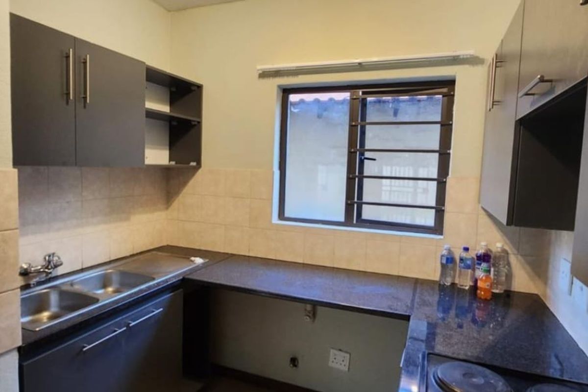 A functional kitchen featuring dark built-in cabinetry, granite countertops, a double basin sink, and an integrated electric hob with tiled backsplash.