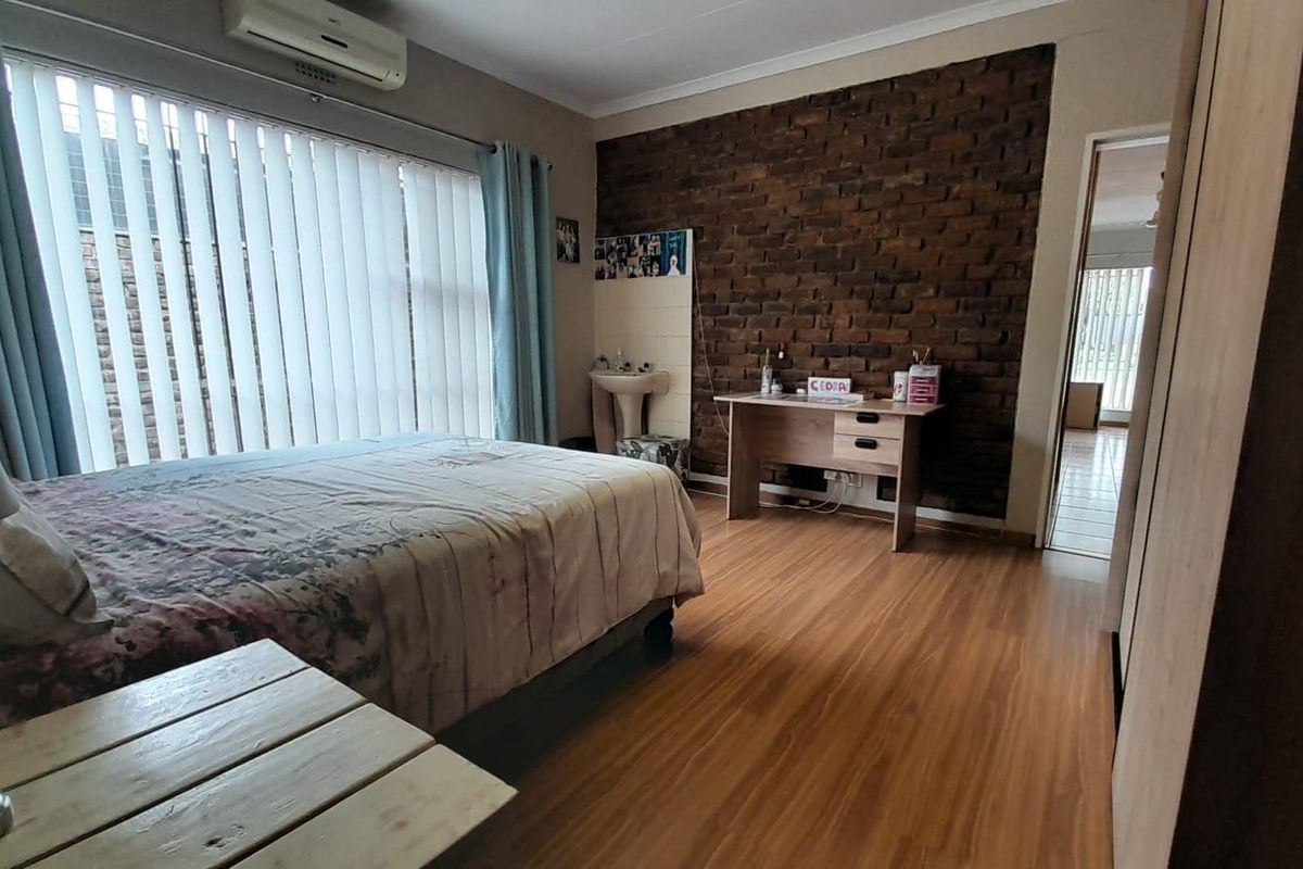 A bedroom featuring wood-look flooring, an exposed brick feature wall, a wall-mounted basin, and a split-system air conditioning unit.