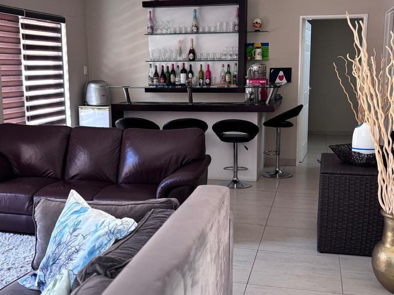 A dedicated home bar area featuring a built-in counter, glass shelving, and tiled flooring, seamlessly integrated into the living space.