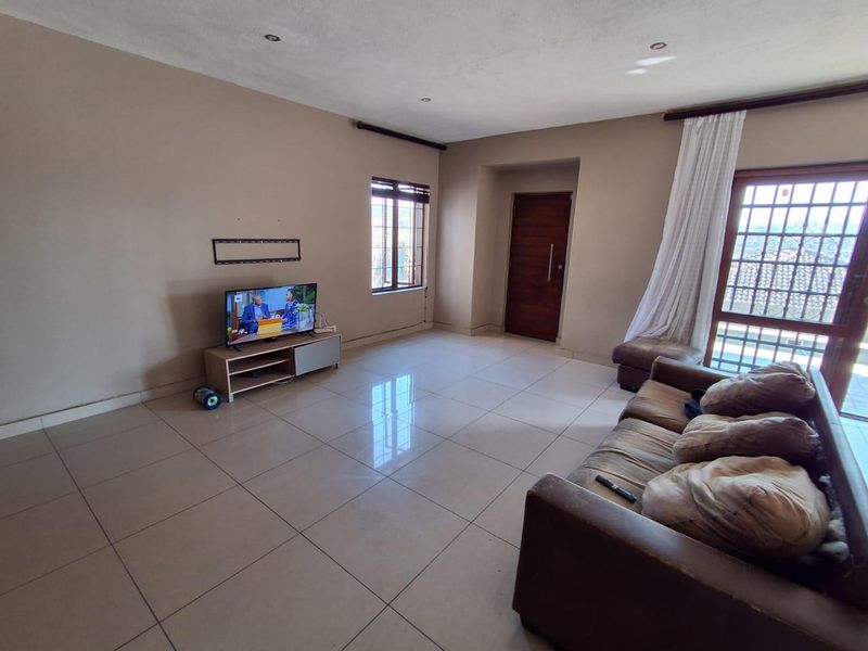 A spacious living room featuring neutral wall tones, large format floor tiles, recessed lighting, and direct access to an outdoor area via a security door.