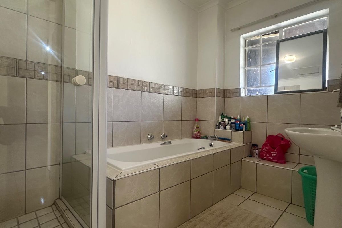 A functional bathroom featuring a built-in bathtub, separate glass-enclosed shower, and a pedestal basin with neutral wall and floor tiling.