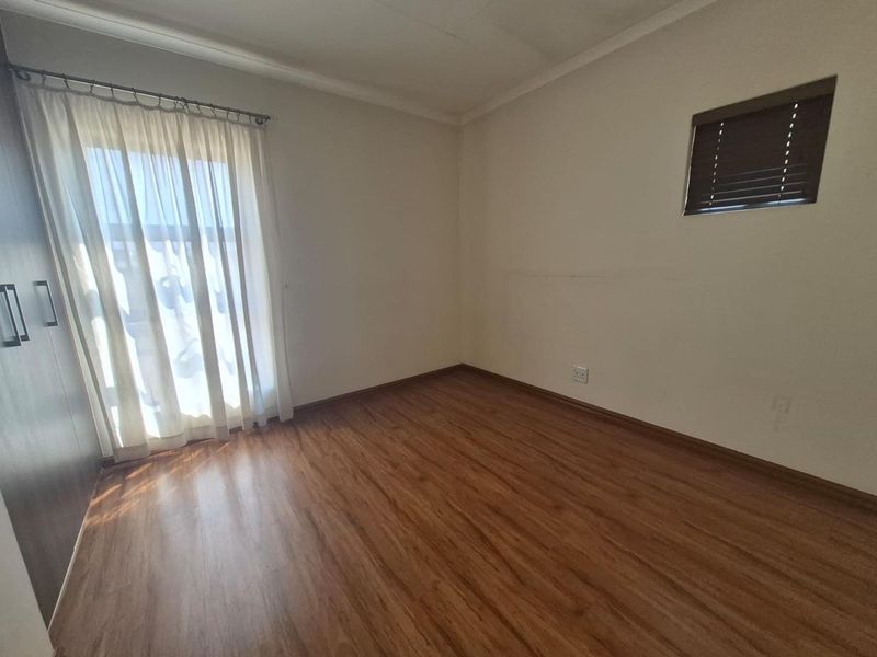 An empty bedroom featuring laminate flooring, built-in cupboards, and a window with a venetian blind.