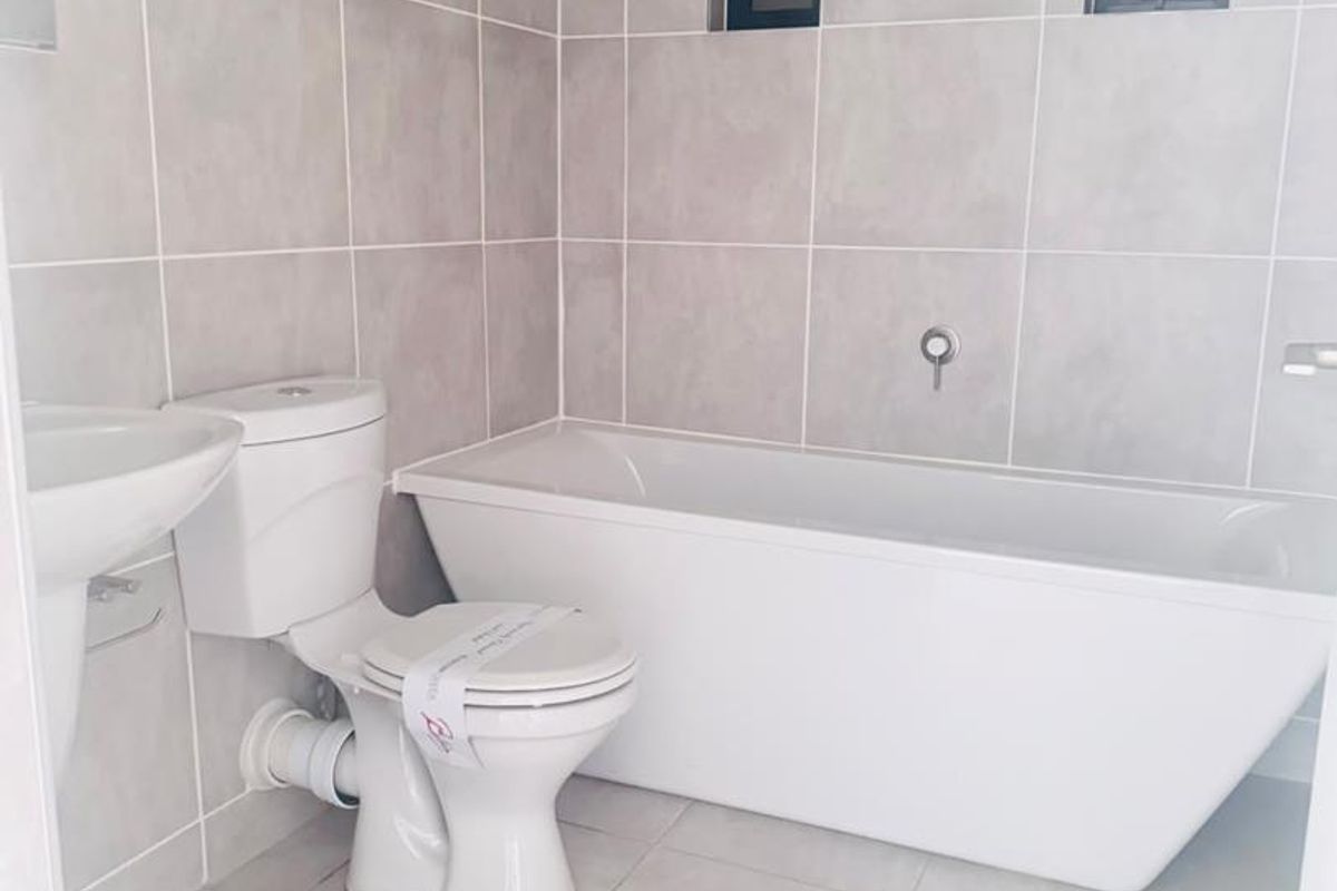 A clean, modern bathroom featuring a freestanding bathtub, pedestal basin, and neutral ceramic tiling throughout.