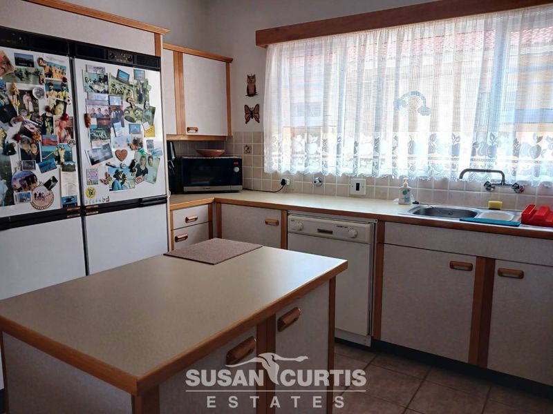 A functional kitchen featuring laminate cabinetry, a central island, tiled backsplash, and a built-in dishwasher, offering potential for modern updates.