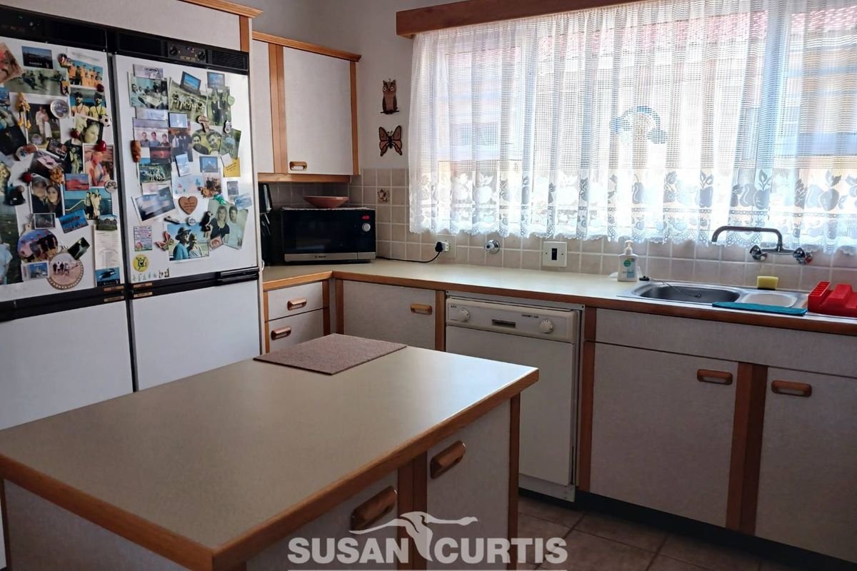A functional kitchen featuring laminate cabinetry, a central island, tiled backsplash, and a built-in dishwasher, offering potential for modern updates.