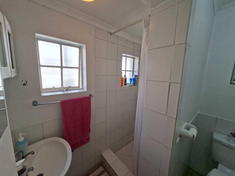 Compact bathroom featuring a pedestal basin, toilet, and a tiled shower cubicle with a curtain.