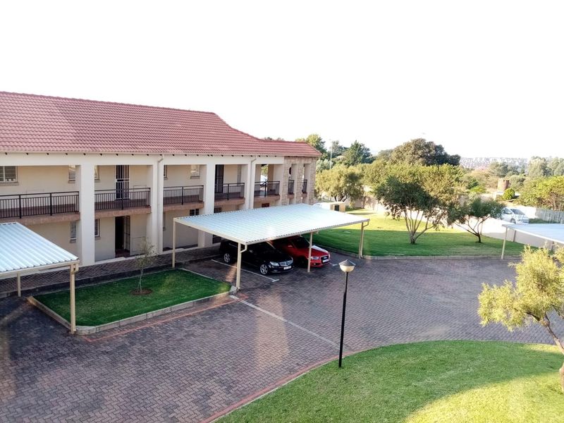 Exterior view of an apartment complex featuring a tiled roof, covered parking bays, paved driveway, and well-maintained communal garden areas.
