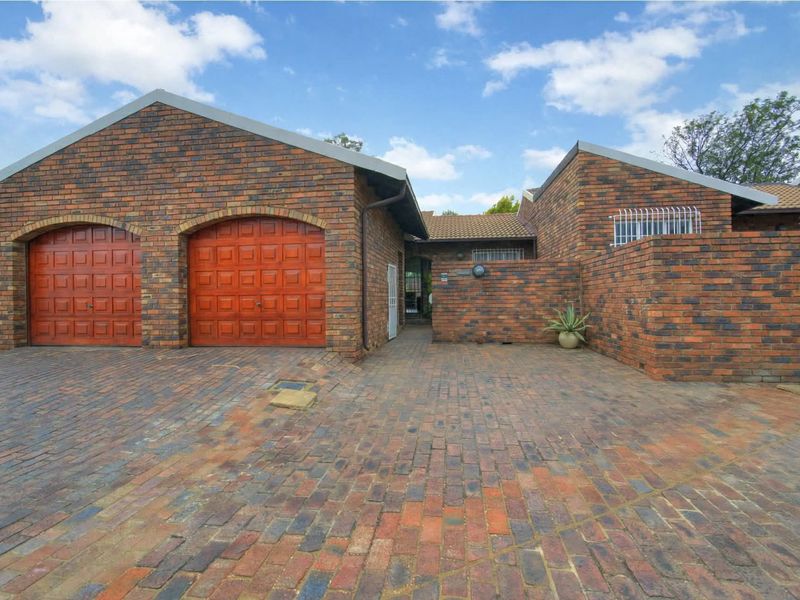 Front exterior view of a townhouse featuring a double garage with wooden doors, a paved brick driveway, and a secure gated entrance.