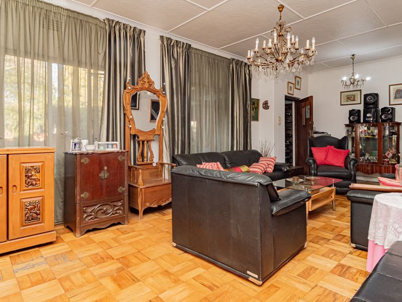 Spacious living room featuring classic parquet flooring, a decorative crystal chandelier, and large sliding glass doors providing natural light.