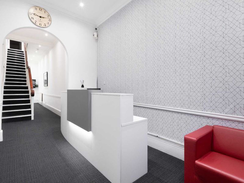Professional office reception area featuring a modern reception desk, arched entryway, and staircase leading to upper levels.