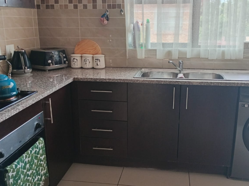 A functional kitchen featuring dark cabinetry, granite countertops, a built-in oven, electric hob, and a double sink with a tiled backsplash.