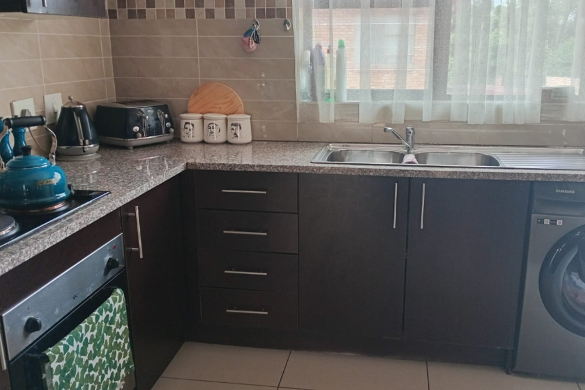 A functional kitchen featuring dark cabinetry, granite countertops, a built-in oven, electric hob, and a double sink with a tiled backsplash.