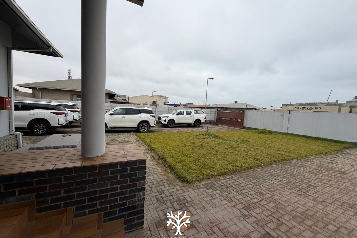 Rear exterior view featuring a paved driveway, lawn area, and secure boundary walling with a sliding gate.