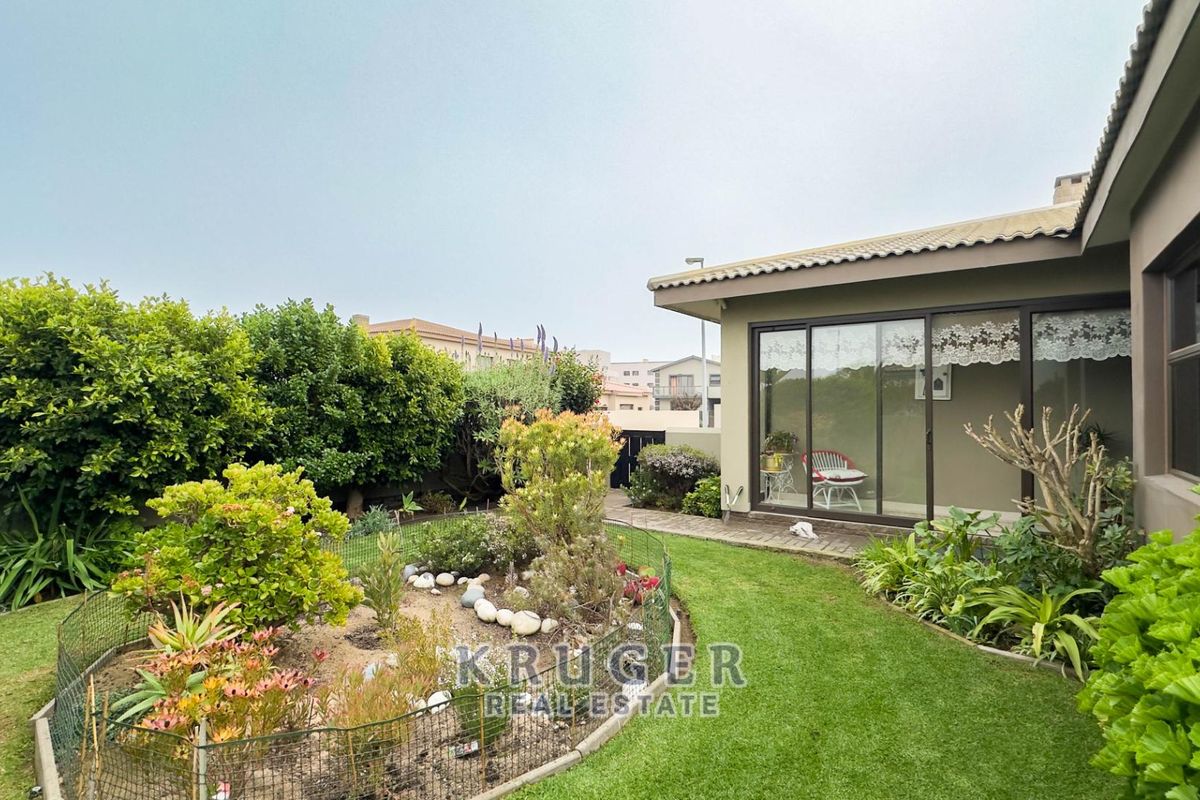 A well-maintained rear garden featuring a paved walkway, established landscaping, and sliding glass doors providing access to the home's interior.