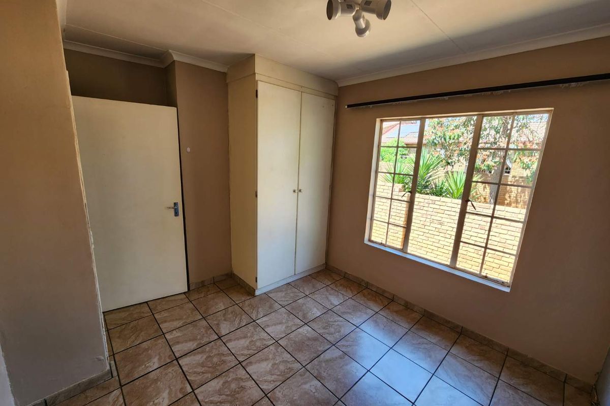 A functional bedroom featuring tiled flooring, a built-in wardrobe, and natural light through a window.