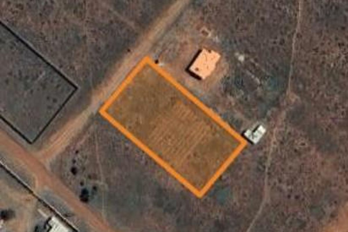 An aerial view of a vacant residential plot with clear boundary markings, situated in a developing area.