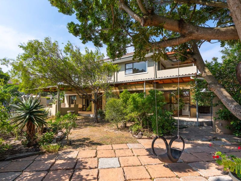 A spacious rear garden featuring a paved patio area, mature trees, and a covered veranda attached to the two-story house.