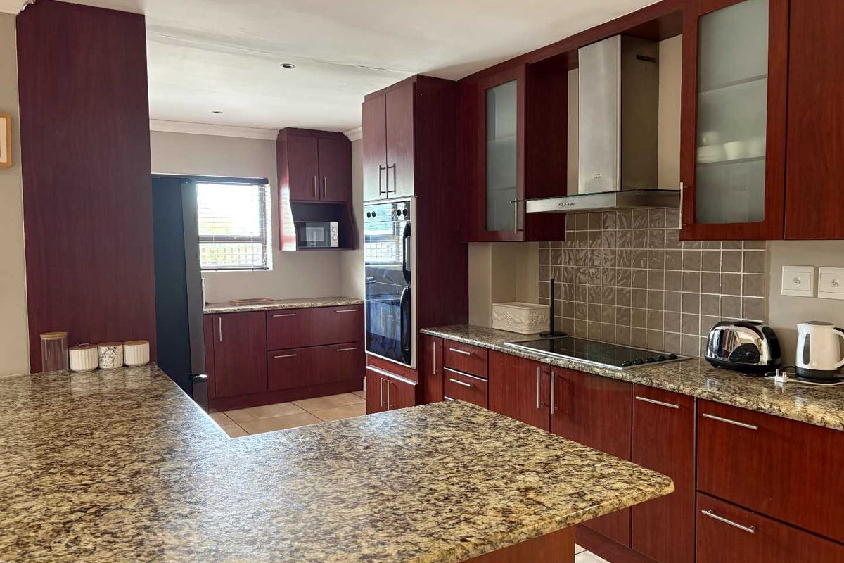A functional kitchen featuring dark wood cabinetry, granite countertops, a built-in oven, and a stainless steel extractor fan.