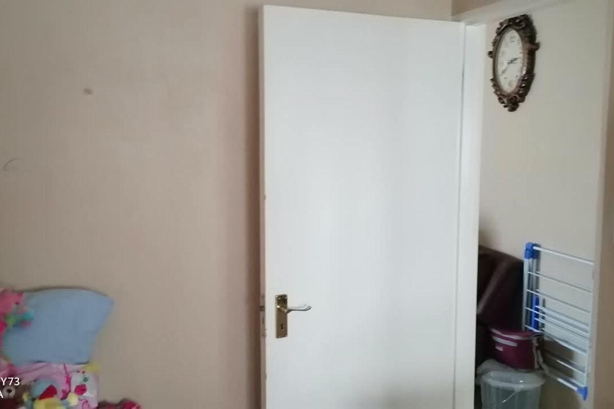 A bedroom interior featuring a standard internal door and wall-mounted light switch, showing signs of wear on the wall surfaces.