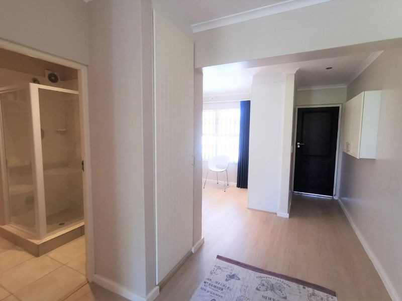 A bright, neutral hallway featuring built-in storage cupboards and direct access to an adjacent bathroom with a shower enclosure.