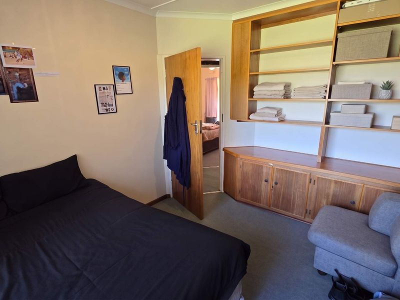 A bedroom featuring built-in wooden cabinetry and shelving, providing ample storage space, with carpeted flooring and access to an adjoining room.