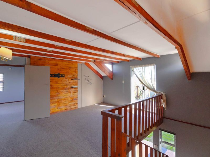 Spacious loft-style living area featuring exposed timber beams, a timber feature wall, and a wooden balustrade overlooking the lower level.