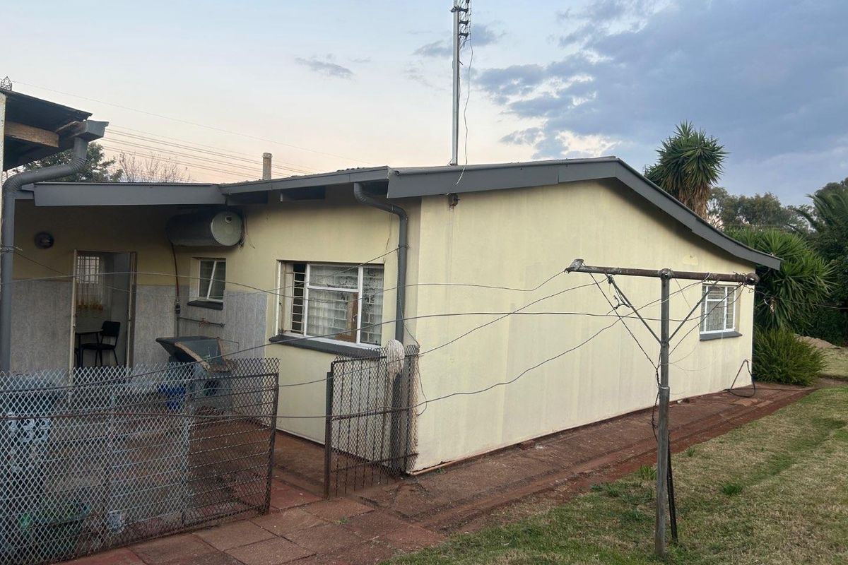 Rear exterior view of the house featuring a paved patio area, metal security fencing, and a fixed outdoor washing line.