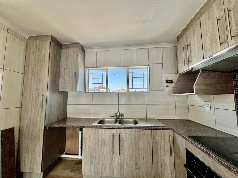 A functional kitchen featuring wood-look laminate cabinetry, granite-style countertops, a double sink, and built-in cooking appliances with tiled splashbacks.