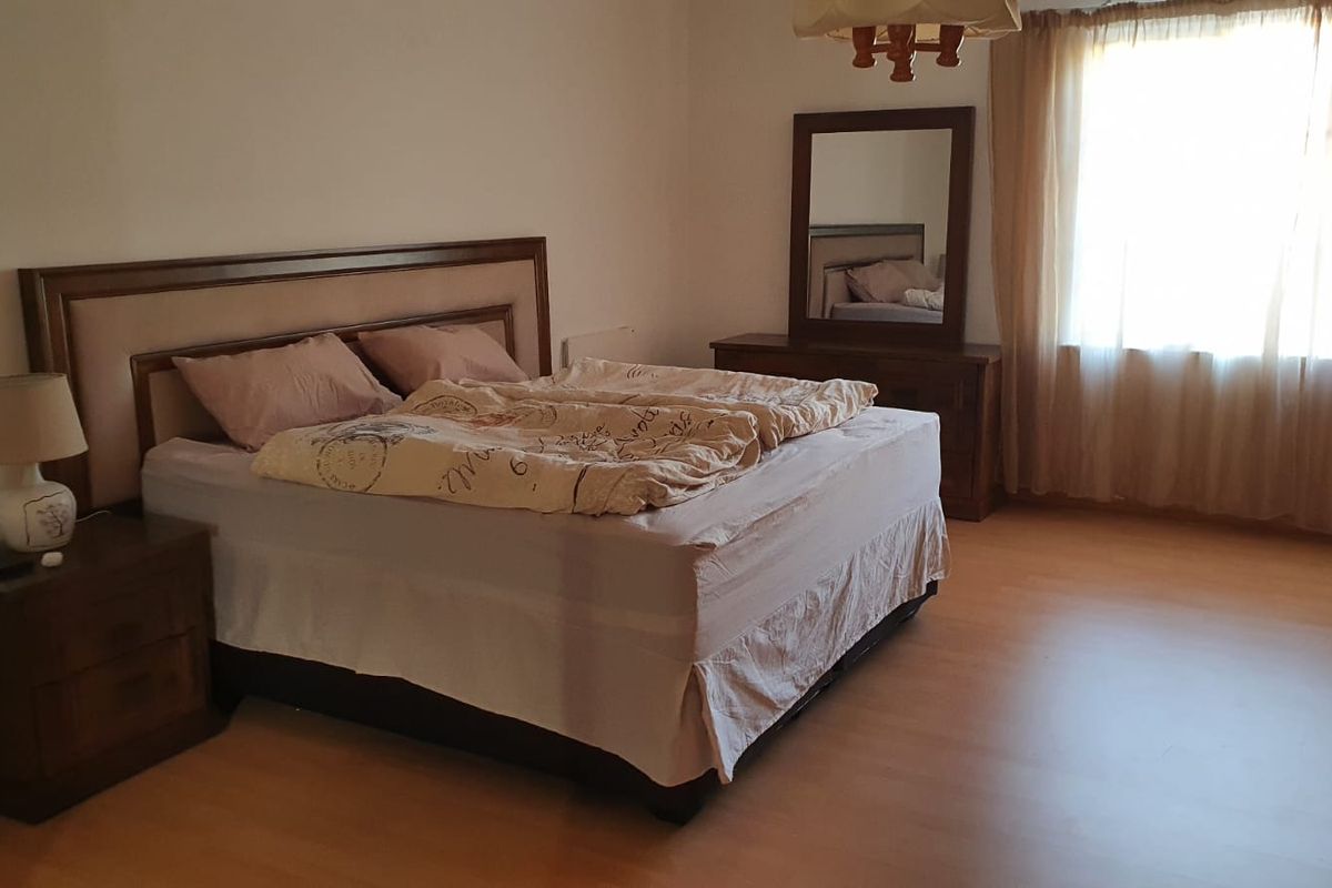 A spacious bedroom featuring laminate flooring and natural light through a large window, offering a neutral canvas for personal interior design updates.