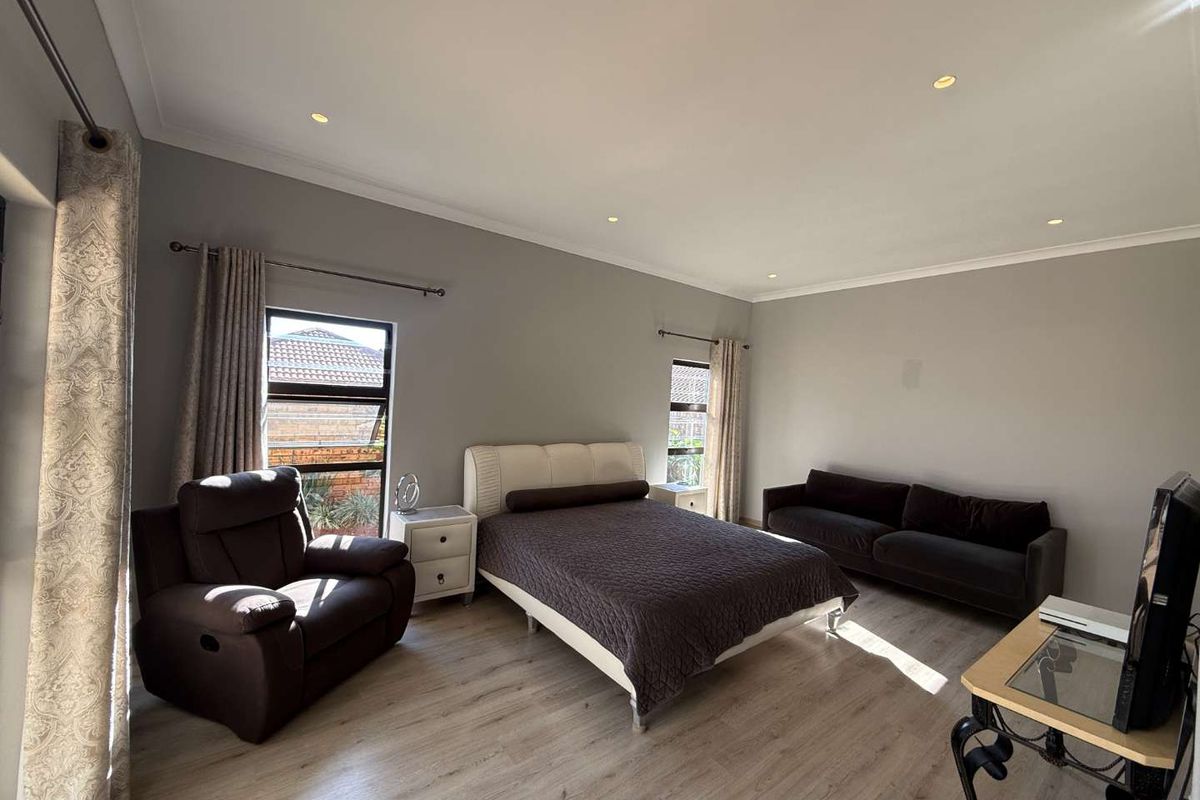 Spacious bedroom featuring modern laminate flooring, recessed downlighting, and large aluminium-framed windows that provide ample natural light.