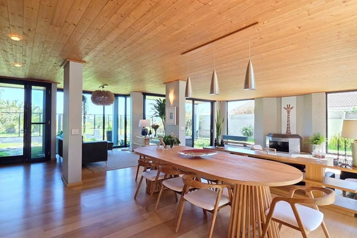 Spacious open-plan living and dining area featuring warm timber ceilings, hardwood flooring, a built-in fireplace, and expansive glass doors leading to the outdoors.
