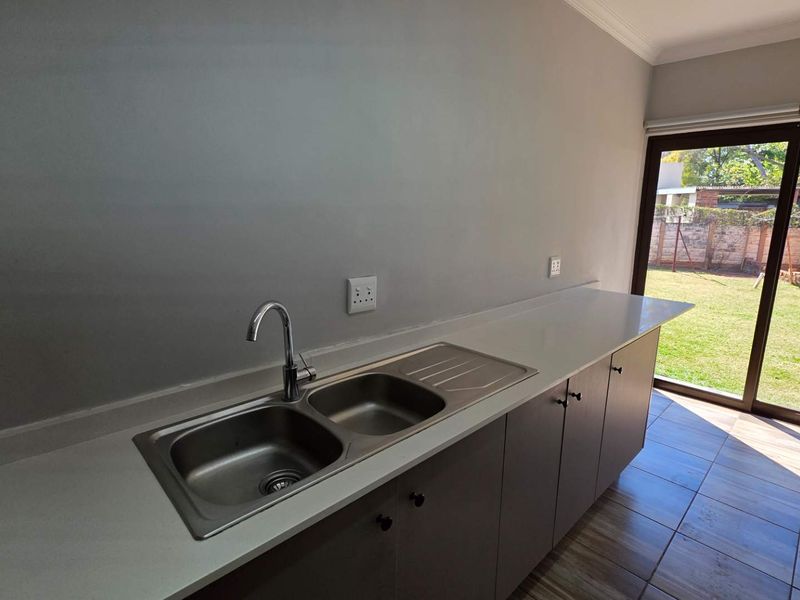 A clean, modern kitchen area featuring a double bowl sink, stone-look countertops, and direct access to the rear garden through a sliding glass door.