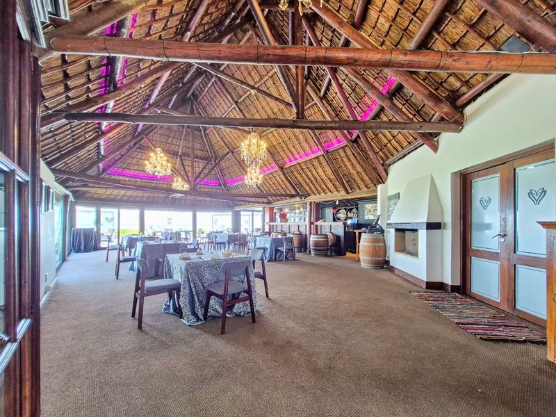 Spacious clubhouse area featuring a high vaulted thatched roof with exposed timber trusses, a built-in fireplace, and a dedicated bar counter.