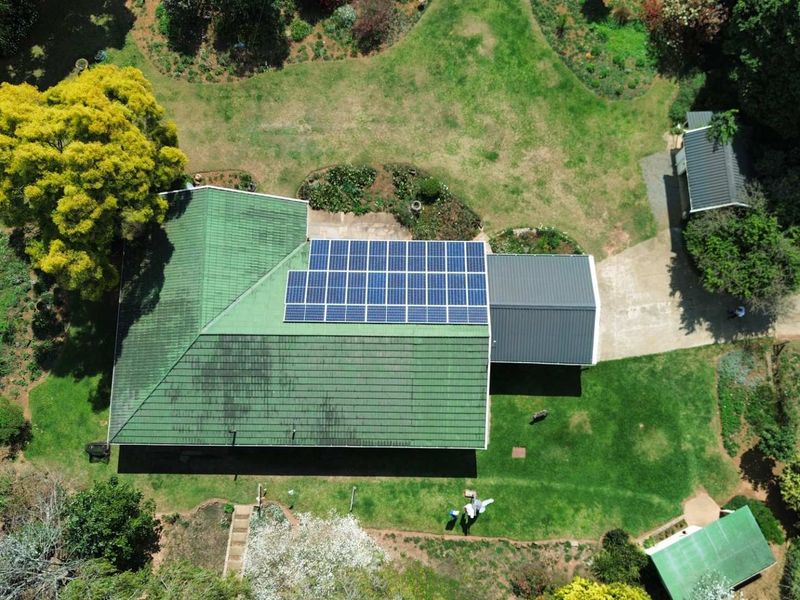 Aerial view of the farm property featuring a main residence with a solar panel installation, metal roofing, and surrounding landscaped garden areas.