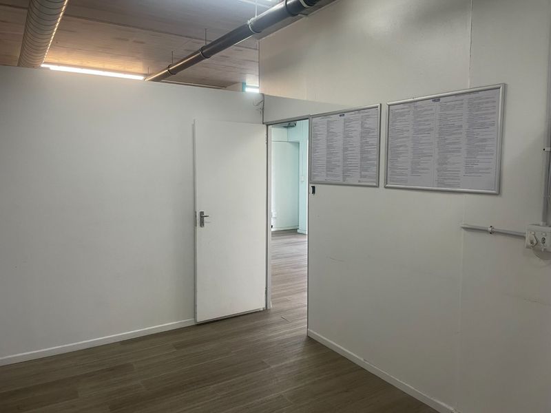 A clean, empty utility or office space featuring laminate flooring, exposed ceiling ducting, and white walls, suitable for various commercial uses.