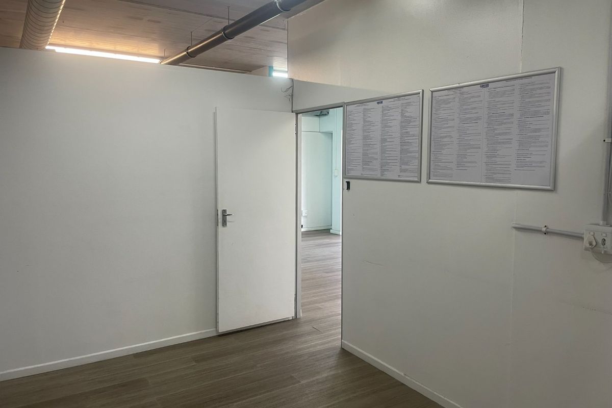 A clean, empty utility or office space featuring laminate flooring, exposed ceiling ducting, and white walls, suitable for various commercial uses.