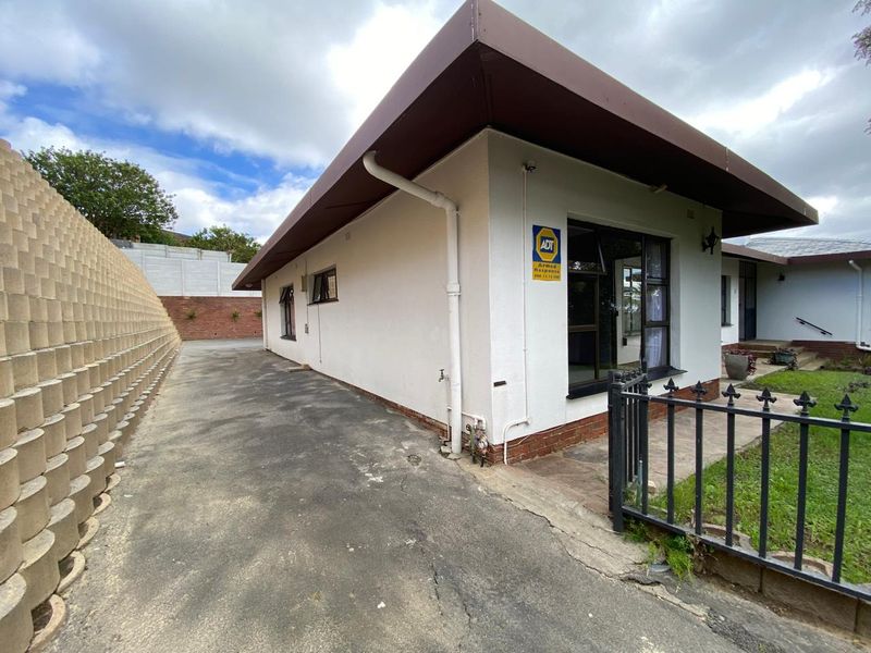 Exterior view of the property featuring a concrete driveway, retaining wall, and metal security fencing along the front facade.