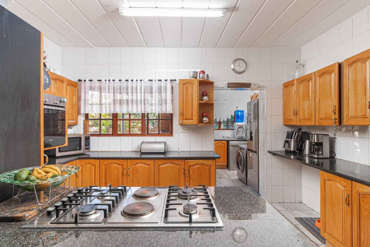 A functional kitchen featuring wooden cabinetry, granite countertops, a built-in gas hob, and an integrated oven, with an adjacent scullery area.