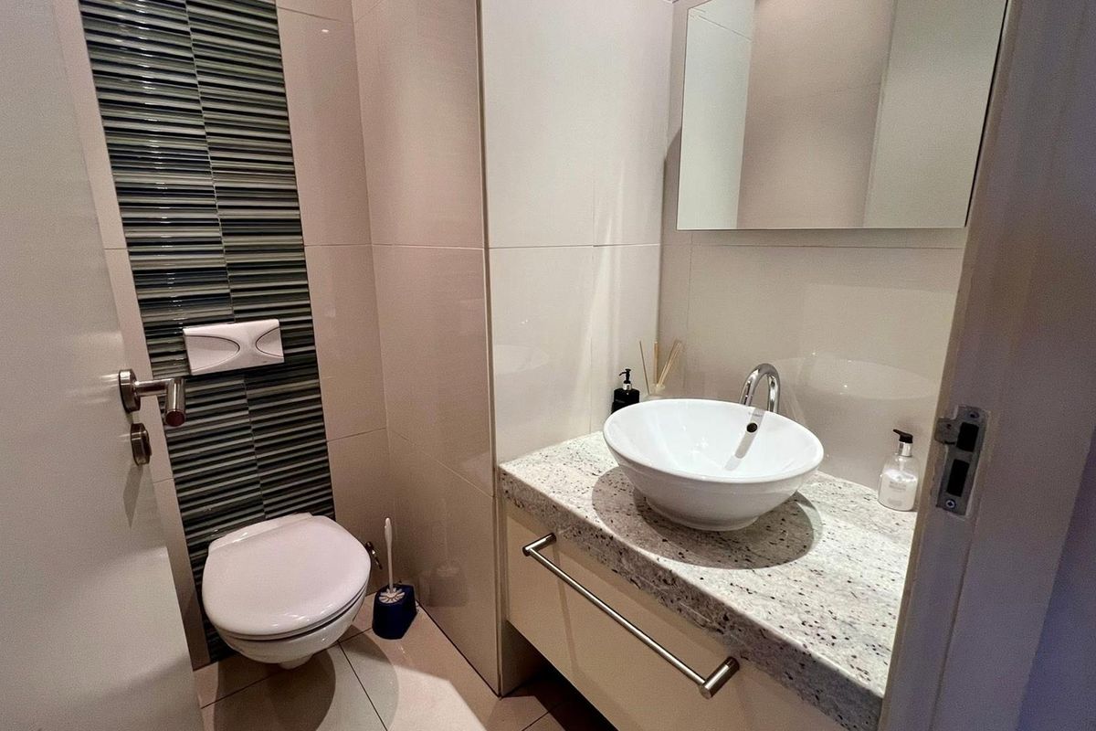 Modern guest bathroom featuring a wall-mounted toilet, vessel sink on a granite vanity countertop, and stylish tiled feature wall.