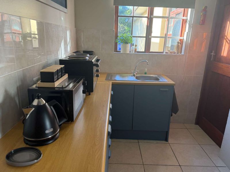 A functional kitchen area featuring laminate countertops, a stainless steel sink, tiled splashbacks, and tiled flooring with natural light from the window.