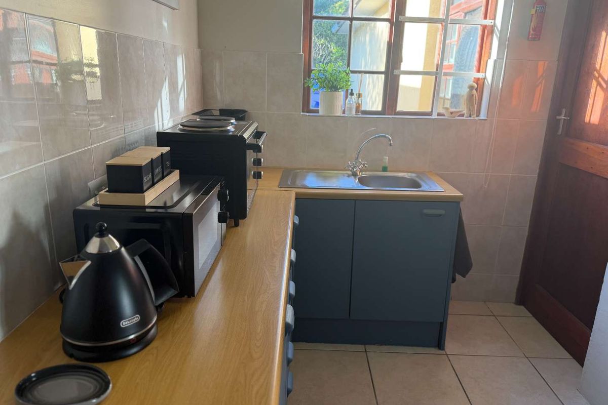 A functional kitchen area featuring laminate countertops, a stainless steel sink, tiled splashbacks, and tiled flooring with natural light from the window.