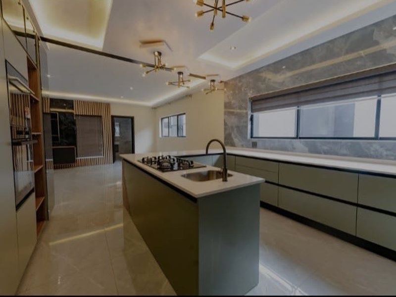 Modern, high-end kitchen featuring a central island with gas hob, stone countertops, integrated appliances, and sophisticated recessed and pendant lighting throughout.