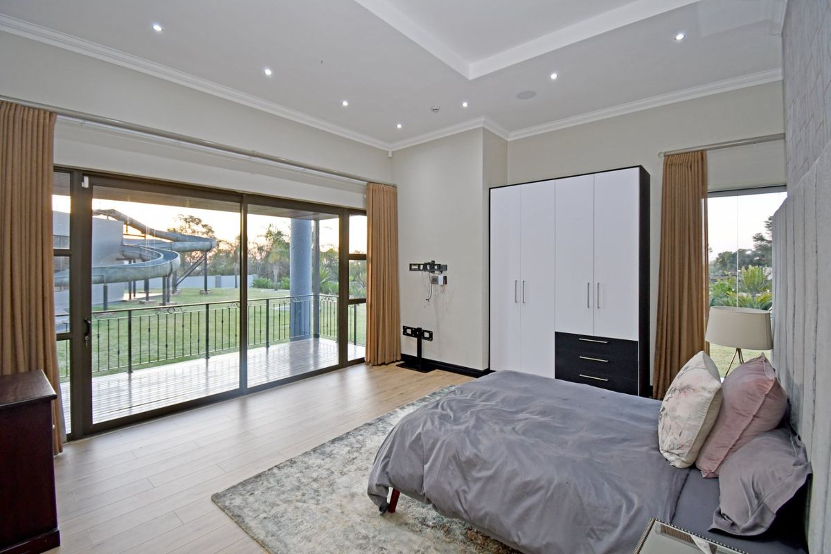 Spacious bedroom featuring modern built-in cupboards, recessed ceiling lighting, and large sliding glass doors opening onto a private balcony with garden views.