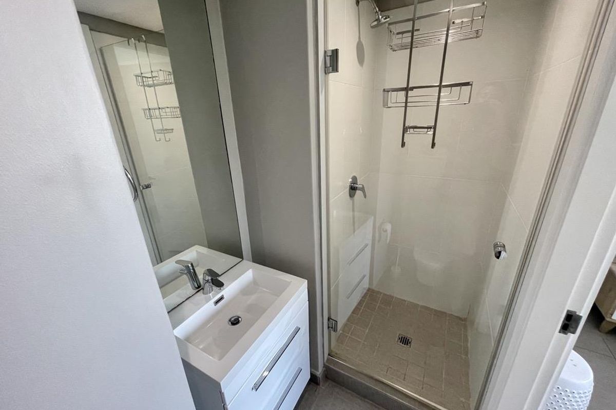 A modern, compact bathroom featuring a sleek vanity with basin, a glass-enclosed shower, and neutral tiled finishes.