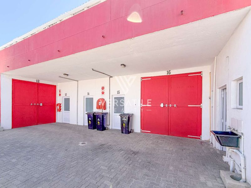 Industrial property exterior featuring multiple numbered access doors, a covered loading bay, and paved driveway area.