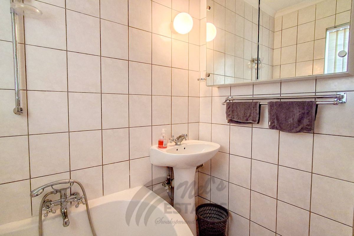 A functional bathroom featuring a pedestal basin, wall-mounted mirror cabinet, and a bathtub with a shower mixer.