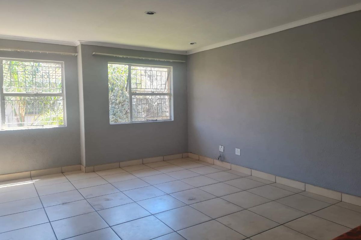 An empty living room featuring neutral grey walls, tiled flooring, and security bars on the windows, offering a blank canvas for personalization.