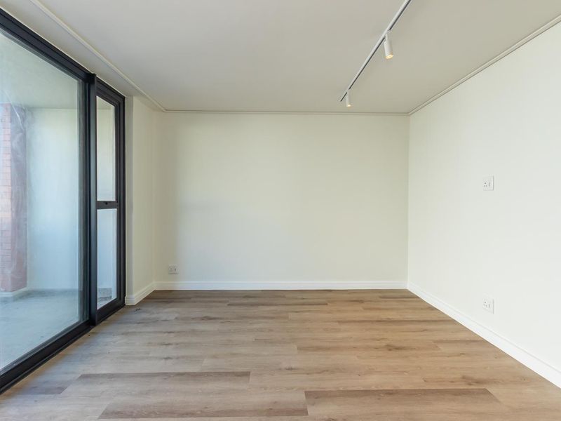 A bright, empty living area featuring modern laminate flooring, track lighting, and a large sliding glass door providing access to an outdoor space.