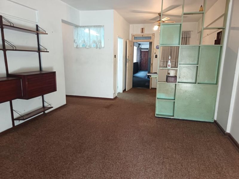 An empty living room featuring carpet flooring, a ceiling fan, and a built-in room divider, offering a blank canvas for renovation.